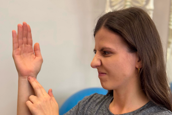 Žena ukazuje a osahává si bolestivé zápěstí – příznaky syndromu karpálního tunelu